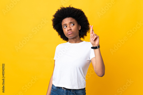 Young African American woman isolated on yellow background with fingers crossing and wishing the best