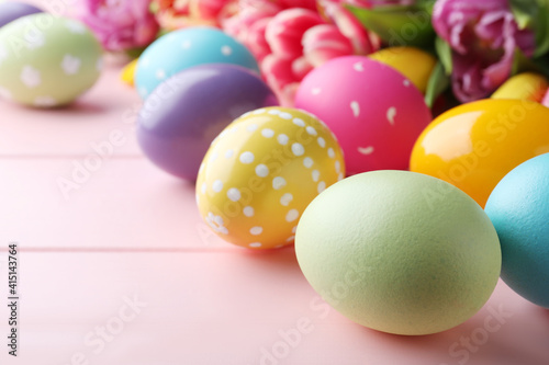 Bright painted eggs and spring tulips on pink wooden table, closeup. Happy Easter