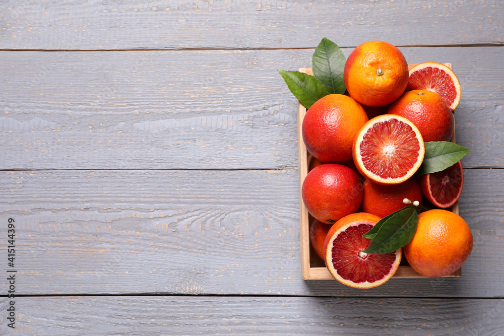 Crate of ripe red oranges and green leaves on grey wooden table, top view. Space for text Crate of ripe red oranges and green leaves on grey wooden table, top view. Space for text