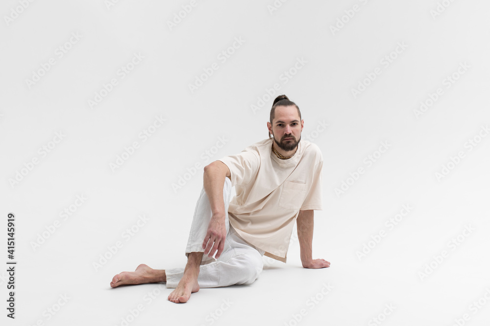 Relaxed young man in white cloath sitting on studio floor isolated on white background
