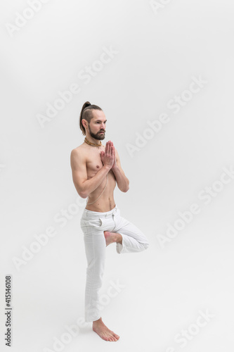 Male yoga teacher practicing in studio. Man isolated on white background stands in asana
