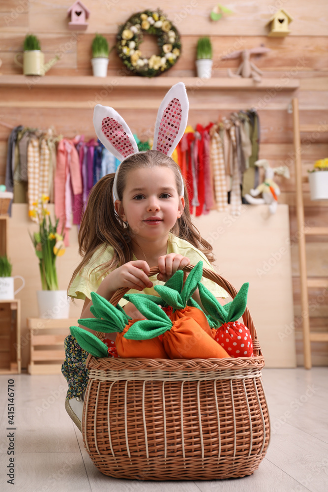 Adorable little girl with bunny ears and basket full of toy carrots in Easter photo zone Adorable little girl with bunny ears and basket full of toy carrots in Easter photo zone