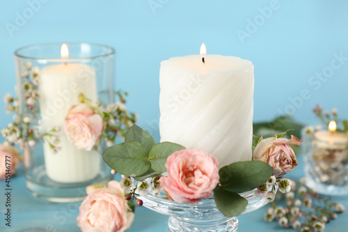 Glass candlestick with burning candles and floral decor on light blue table, closeup