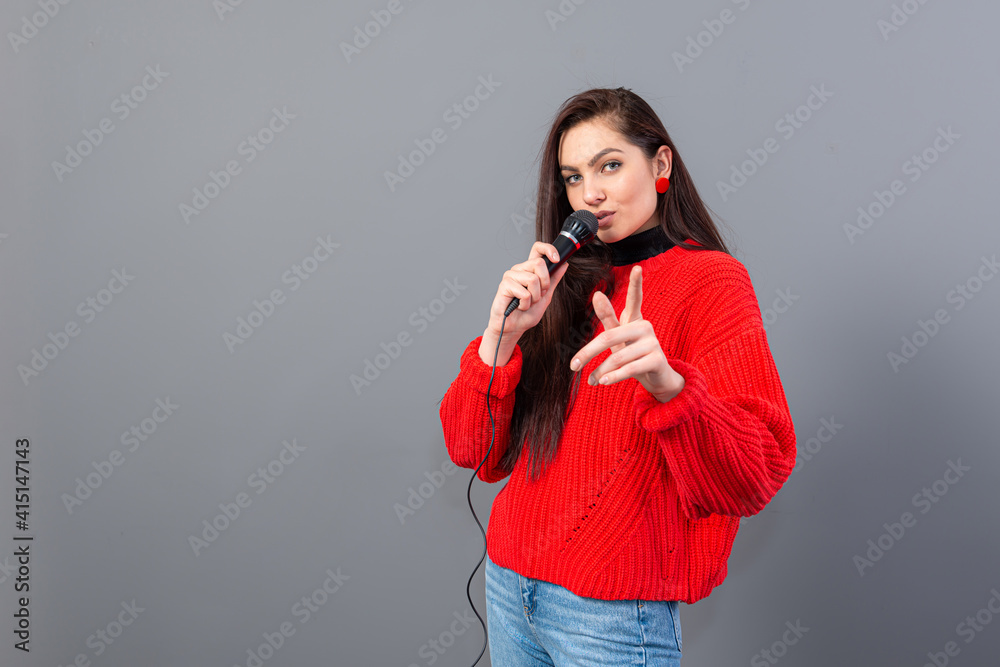 young, emotional brunette with a microphone dressed in a red sweater sings karaoke or says a speech young, emotional brunette with a microphone dressed in a red sweater sings karaoke or says a speech