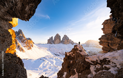 Hiker on rocks admiring Tre Cime di Lavaredo and Monte Paterno covered with snow at sunset, Sesto Dolomites, South Tyrol