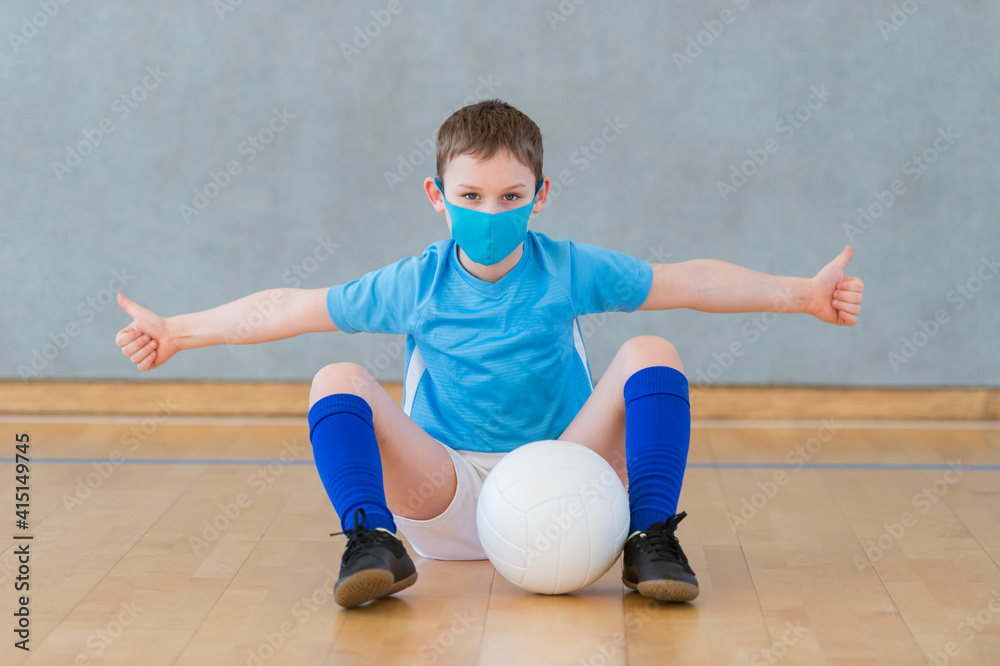 Naklejka premium School kid with mask and volleyball ball in a physical education lesson. Social distancing to fight COVID-19. Safe back to school during pandemic concept