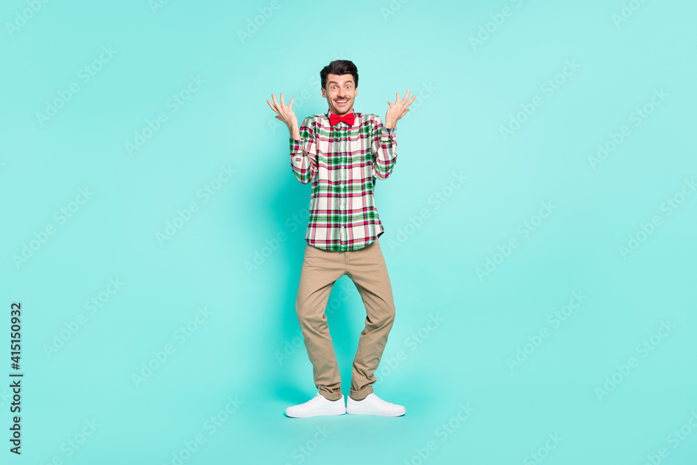 Photo of funny clueless guy raise hands look camera wear checkered shirt pants shoes isolated blue color background Photo of funny clueless guy raise hands look camera wear checkered shirt pants shoes isolated blue color background
