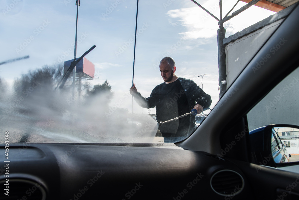 Lavado de coches. Vista desde el interior del automóvil de un hombre que  limpia el cristal