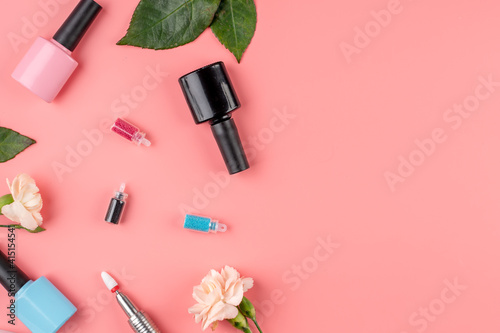 Colorful bottles of nail polishes and tools and accessories for manicure and pedicure procedures on a pink background. Top view and copy space