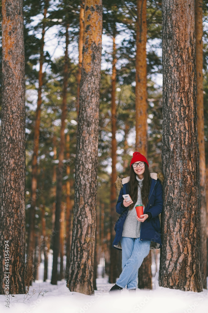 Smiling caucasian girl with paper cup and phone in the forest. Walking with cup off coffe. Spring is coming. Happy smile Smiling caucasian girl with paper cup and phone in the forest. Walking with cup off coffe. Spring is coming. Happy smile