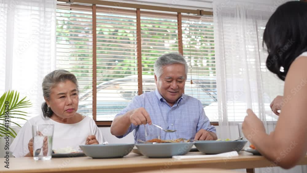 Asian family having dinner together at home. Smiling adult couple with senior parents enjoy eating and sharing thai food on dining table. Happy family spending time together on weekend vacation. Asian family having dinner together at home. Smiling adult couple with senior parents enjoy eating and sharing thai food on dining table. Happy family spending time together on weekend vacation.