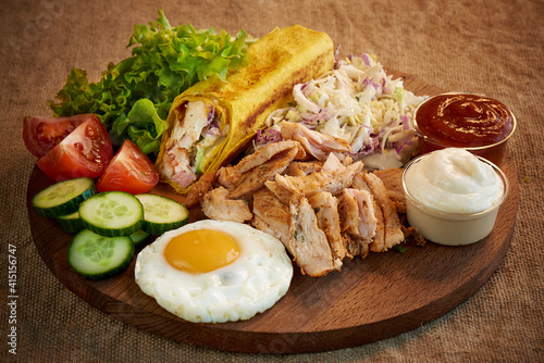 Shawarma with meat, fresh vegetables and scrambled eggs on a wooden cutting board.