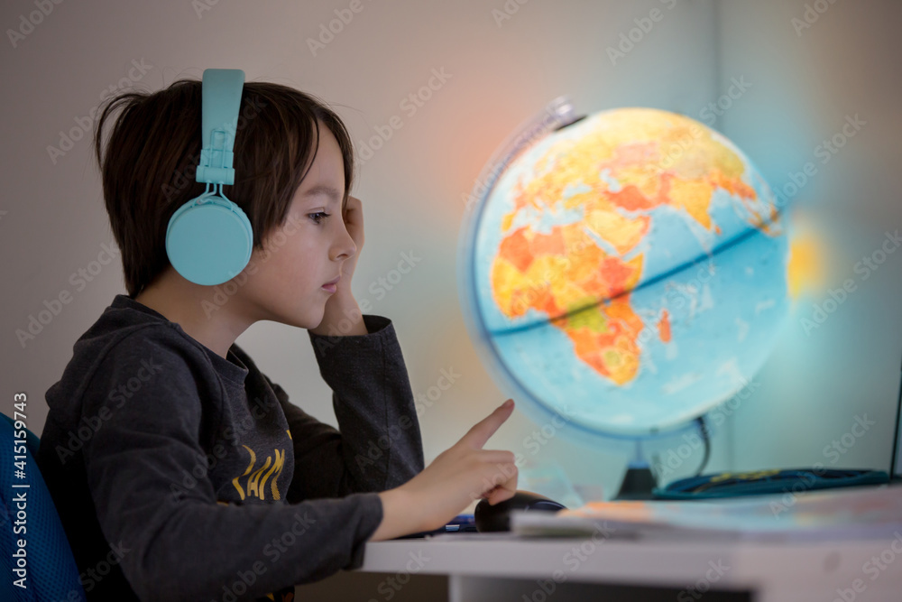 Beautiful child with earphones using laptop while studying at desk at home Beautiful child with earphones using laptop while studying at desk at home