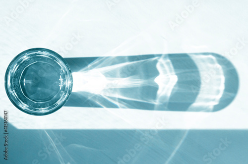 A glass with clean clear water and sharp shadows stands on a white table