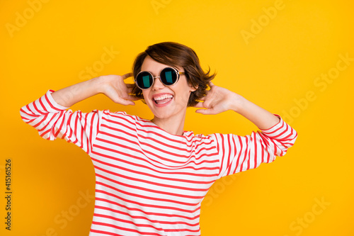 Photo of young beautiful positive excited smiling cheerful girl in sunglasses dancing isolated on yellow color background