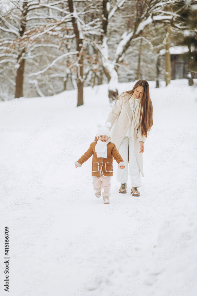 Beautiful mother with daughter walking together in a winter park