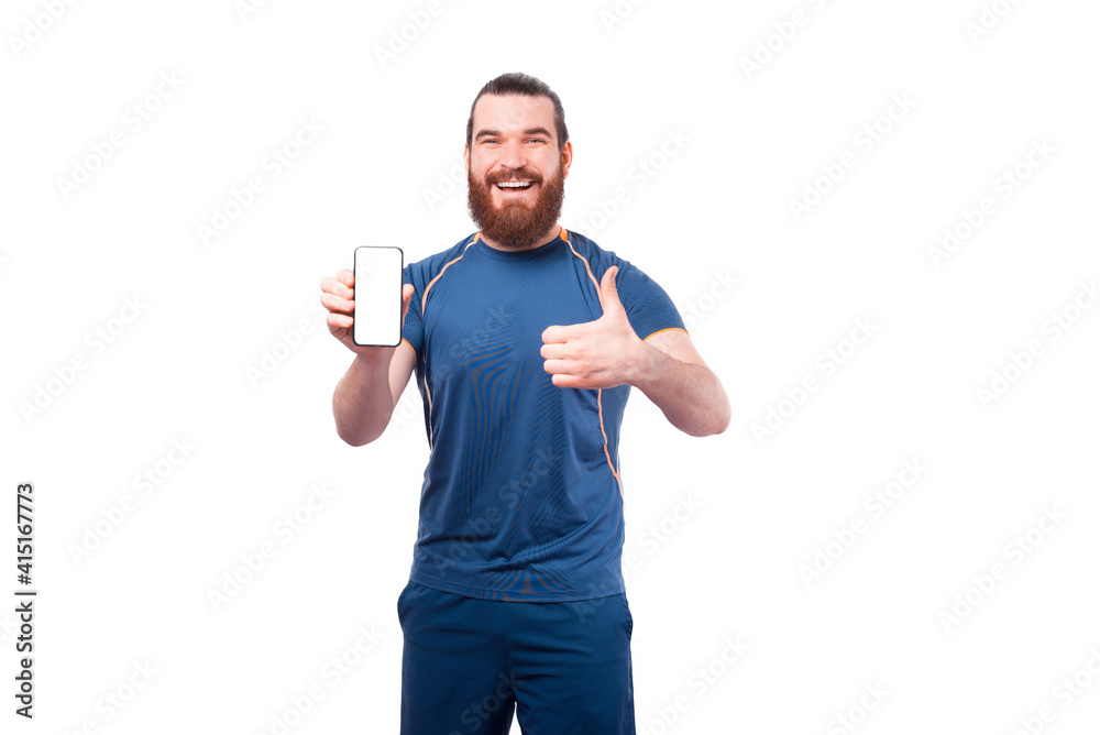 Cheerful young fitness man showing white screen on smartphone and thumb up. Cheerful young fitness man showing white screen on smartphone and thumb up.