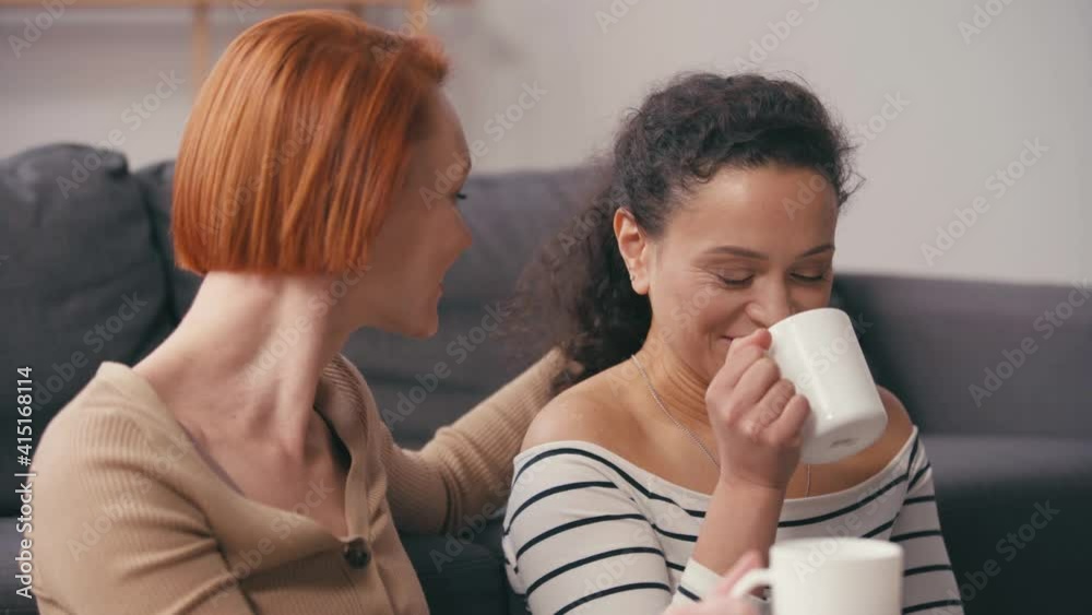 redhead woman touching hair and talking with hispanic girlfriend drinking coffee redhead woman touching hair and talking with hispanic girlfriend drinking coffee