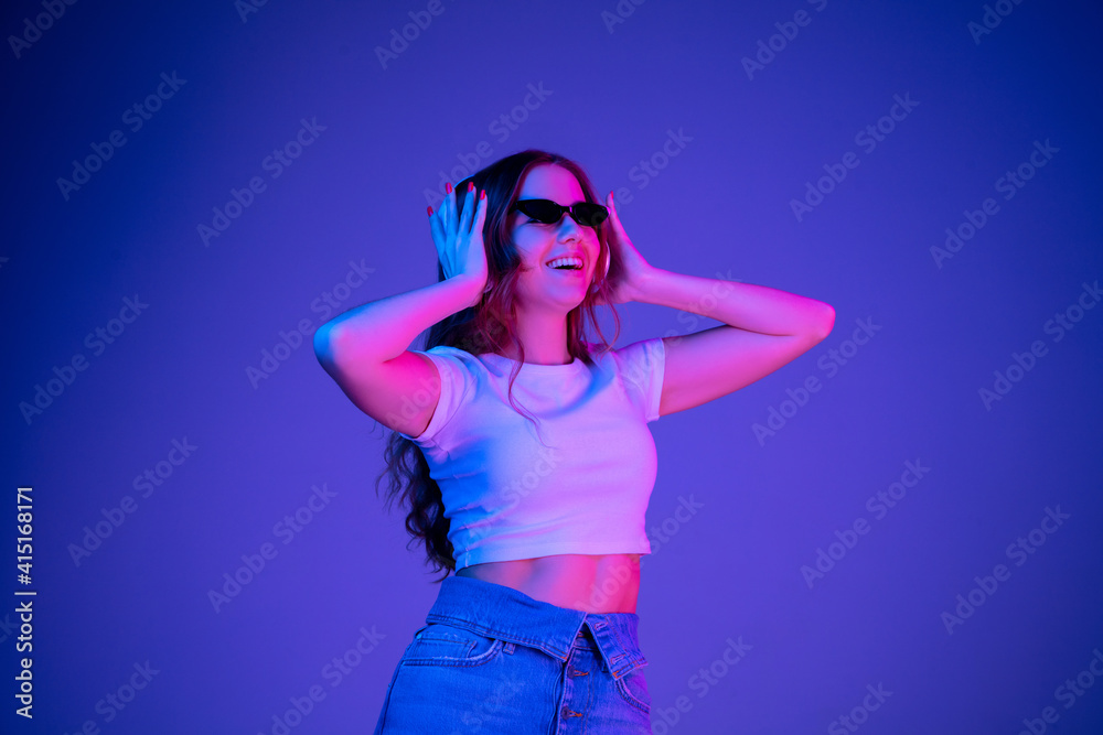 Caucasian woman's portrait isolated on blue studio background in multicolored neon light. Beautiful model with headphones. Concept of human emotions, facial expression, sales, ad, fashion. Copyspace. Caucasian woman's portrait isolated on blue studio background in multicolored neon light. Beautiful model with headphones. Concept of human emotions, facial expression, sales, ad, fashion. Copyspace.