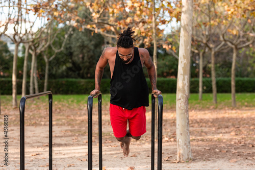 african american athlete boy does calisthenics fitness exercises on bars in park