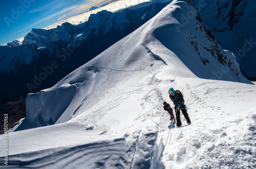 climber on the top of mountain going up by the rope with Himalayan peaks panorama 