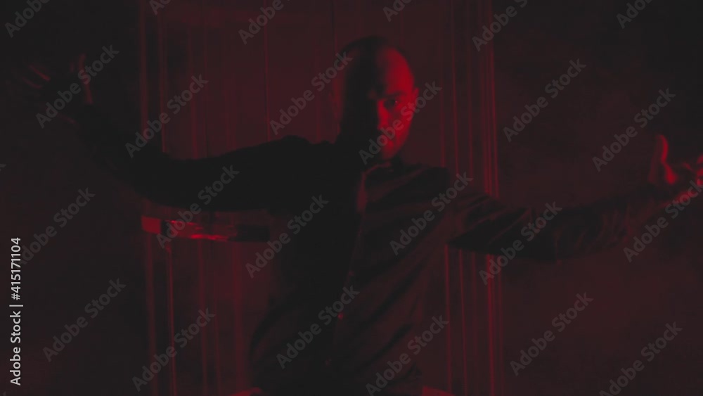 Man in black in red light in smoke near the metal cage Man in black in red light in smoke near the metal cage