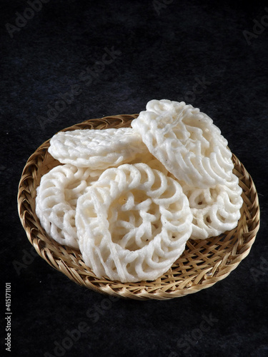 Kerupuk putih or kerupuk warung is Indonesian traditional deep fried crackers made from starch mixed with flavorings such as fish, served in wicker plate. Isolated against black background. photo