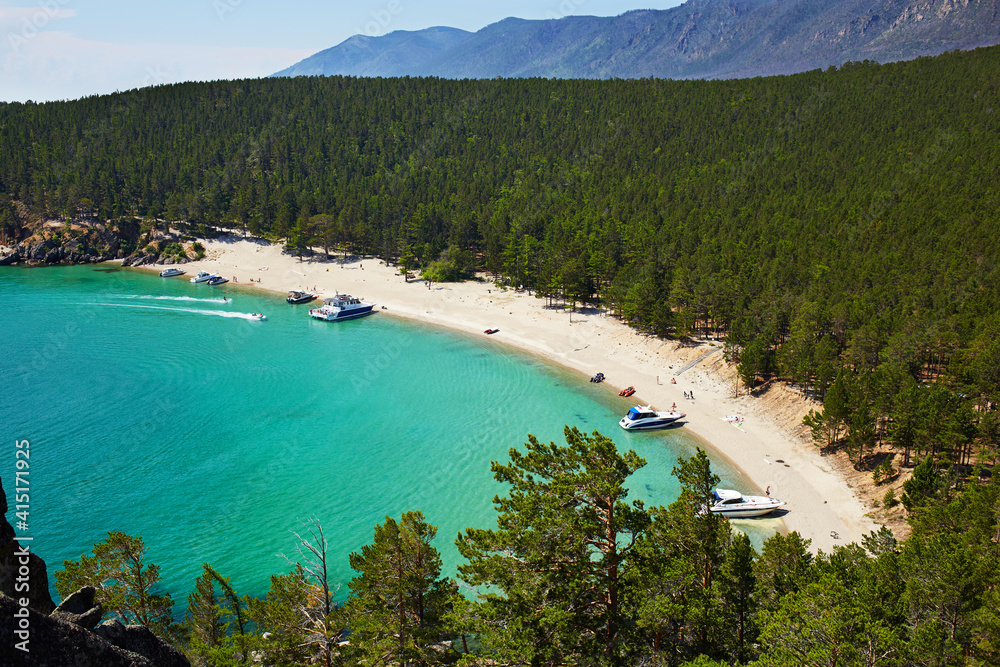 The beautiful sandy beach on summer sunny day. Lake Baikal, the Sandy Bay. Yachts near the shore, tourists sunbathe