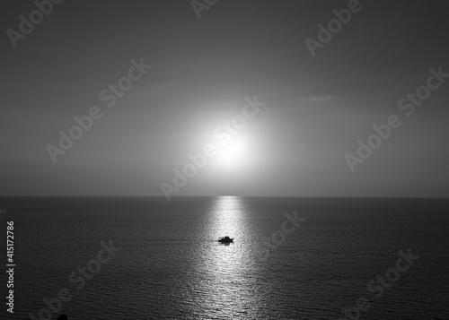 Photos of the boat on the ocean in the evening. Sunshine on water as glistening light with black and white color. There is a horizon line behind. The idea for monochrome background with copy space.