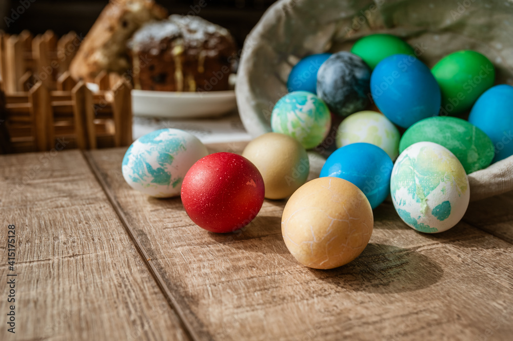 Basket with colored Easter eggs and Easter cake lie on a brown wooden surface Basket with colored Easter eggs and Easter cake lie on a brown wooden surface