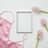 Styled feminine flat lay with blank photo frame, silk lingerie and pink flowers on white background. top view, copy space. 