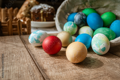 Basket with colored Easter eggs and Easter cake lie on a brown wooden surface