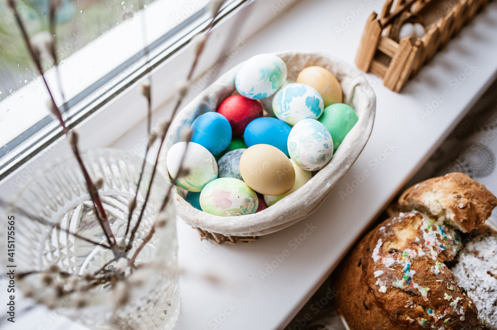 Fototapeta premium Willow branches in a vase, colored eggs in a basket on the windowsill and a festive Easter cake