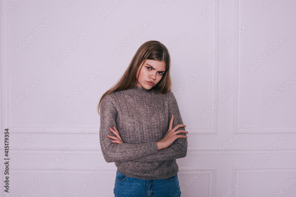 Frowning woman with folded hands near white wall