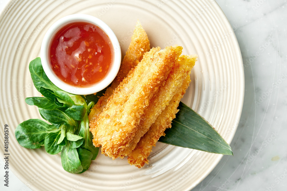 Asian street food - Deep-fried spring roll in rice paper served in a beige plate with spicy chili sauce on a marble background. Restaurant food. Asian street food - Deep-fried spring roll in rice paper served in a beige plate with spicy chili sauce on a marble background. Restaurant food.