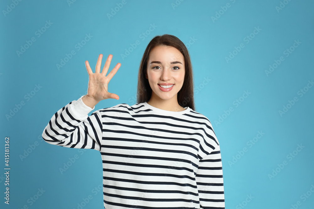 Woman showing number five with her hand on light blue background Woman showing number five with her hand on light blue background