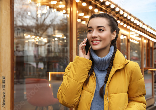 Young woman talking on mobile phone near cafe decorated for Christmas