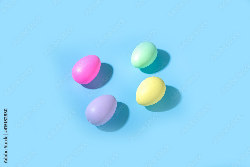 Creative simple pattern made of colorful bright Easter eggs with hard light on blue background. Minimal Easter holiday concept