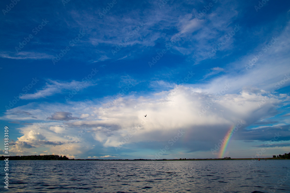 Rainbow over the river after rain on the background of blue sky in summer