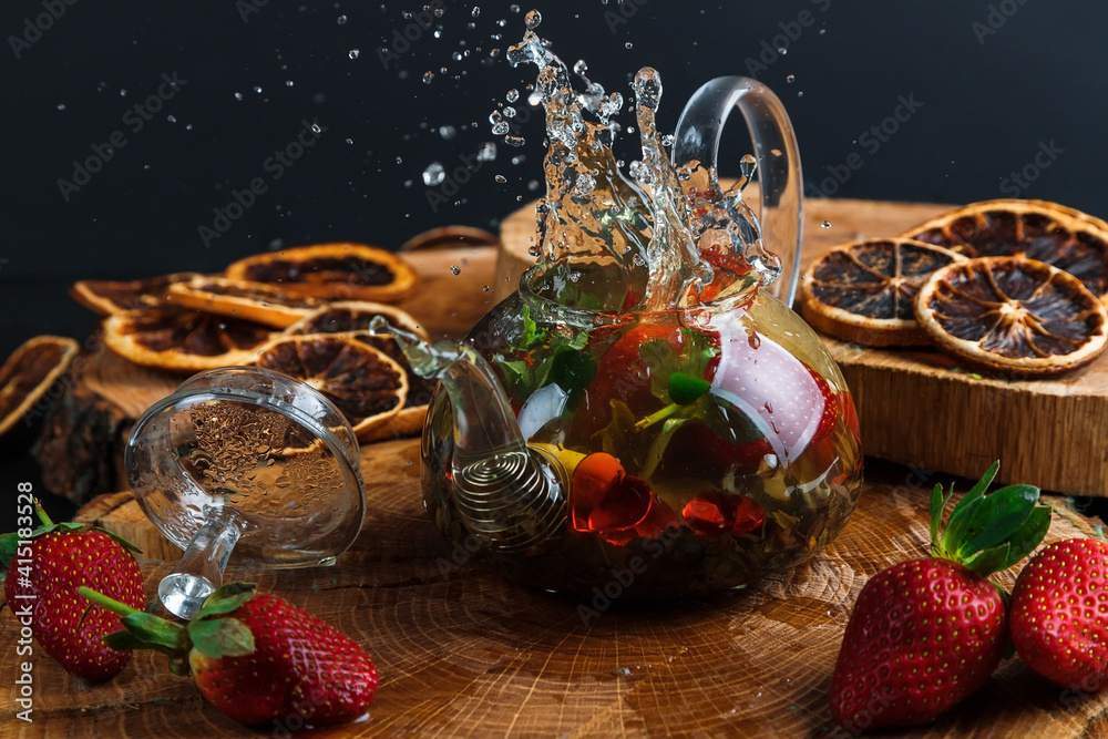 Hot tea with lemon and strawberries. Glass teapot. Wooden stand. Splash.