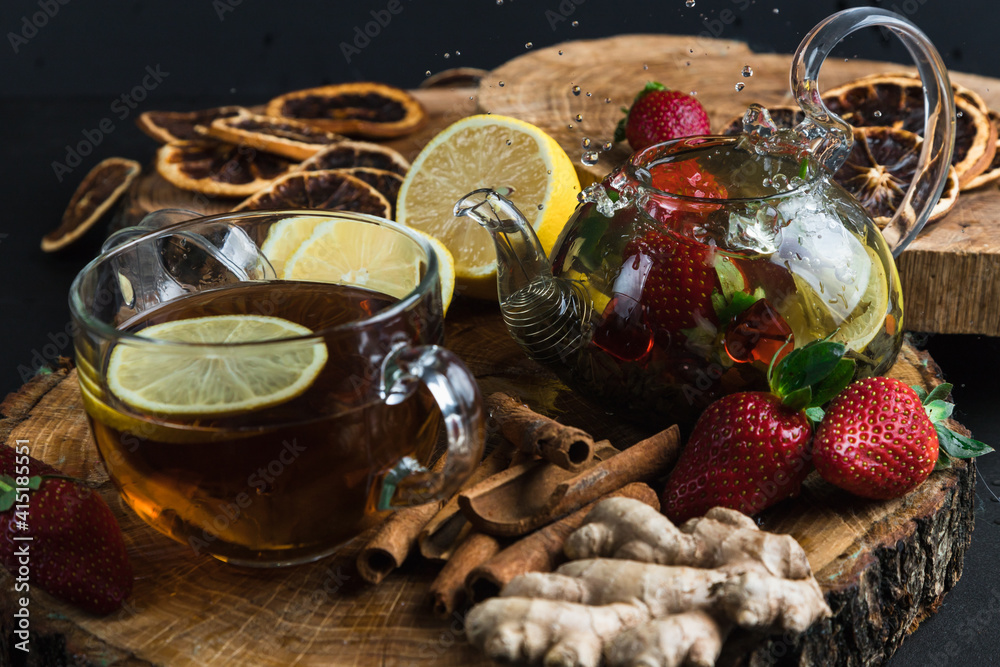 Glass teapot. Still life with hot tea with lemon and strawberries. Wooden stand. Splash.