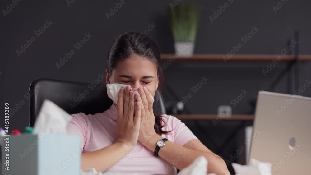 Woman at workplace wipes her nose with napkin. Allergy, coronavirus. Young girl having a flu, sneezing and runny nose. Brunette female taking napkin from tissue box while sitting at home. Close up.