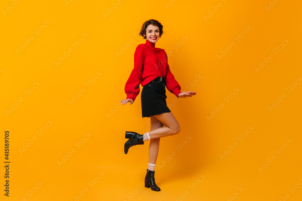Positive girl with short hair dancing on yellow background. Studio shot of happy slim woman in red sweater.