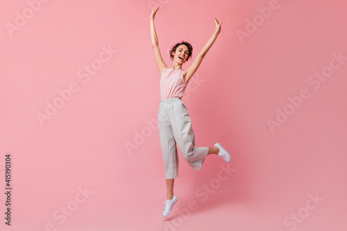 Blithesome french woman in pants jumping with hands up. Studio shot of lovely girl in beret.