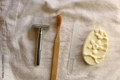 Sustainable toiletries on linen cloth: reusable metal safety razor, wooden toothbrush, glass nail file and soap bar. Top view.