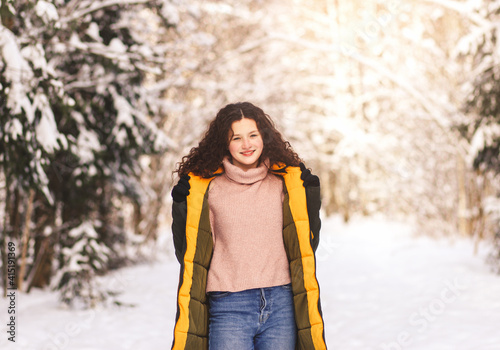 Beautiful young girl walks in the sunny winter forest