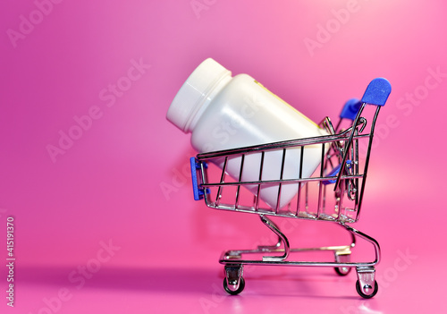 Pills in plastic bottle in shopping cart. Medicine grade pharmaceutical tablets at mini shopping trolley. Medical pill for maintaining and improving health in shopping basket cart