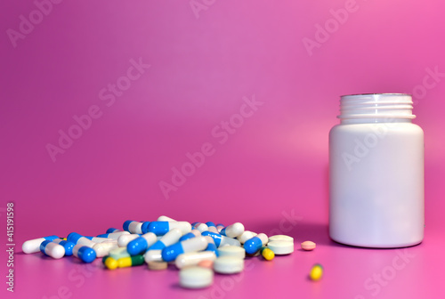 Multicolored Pills with plastic bottle on pink background. Medicine grade pharmaceutical tablets. Medical pill for maintaining and improving health