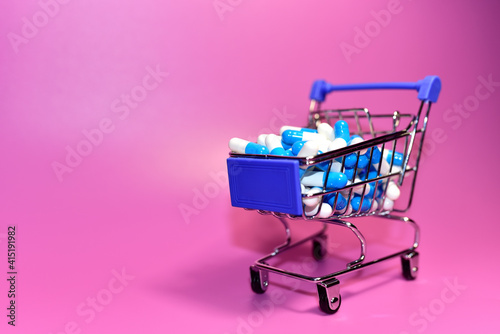 Pills in capsules and shopping cart. Medicine grade pharmaceutical tablets at mini shopping trolley. Medical pill for maintaining and improving health. Financial and economic concept