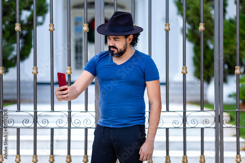 Homem com chapéu na cabeça e camiseta azul, usando aparelho celular. photo